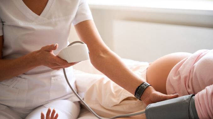 Female doctor checking blood pressure of pregnant woman during pregnancy